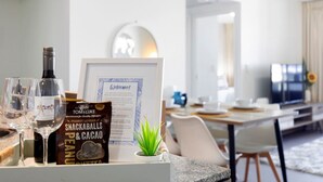 Une chambre d’hôtel avec un coin repas, un panneau d’accueil encadré, une bouteille de vin, un panneau indiquant la présence d’un bar servant des collations et une petite plante posée sur le comptoir.