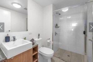 A modern bathroom with a white sink, toilet, and glass-enclosed shower.