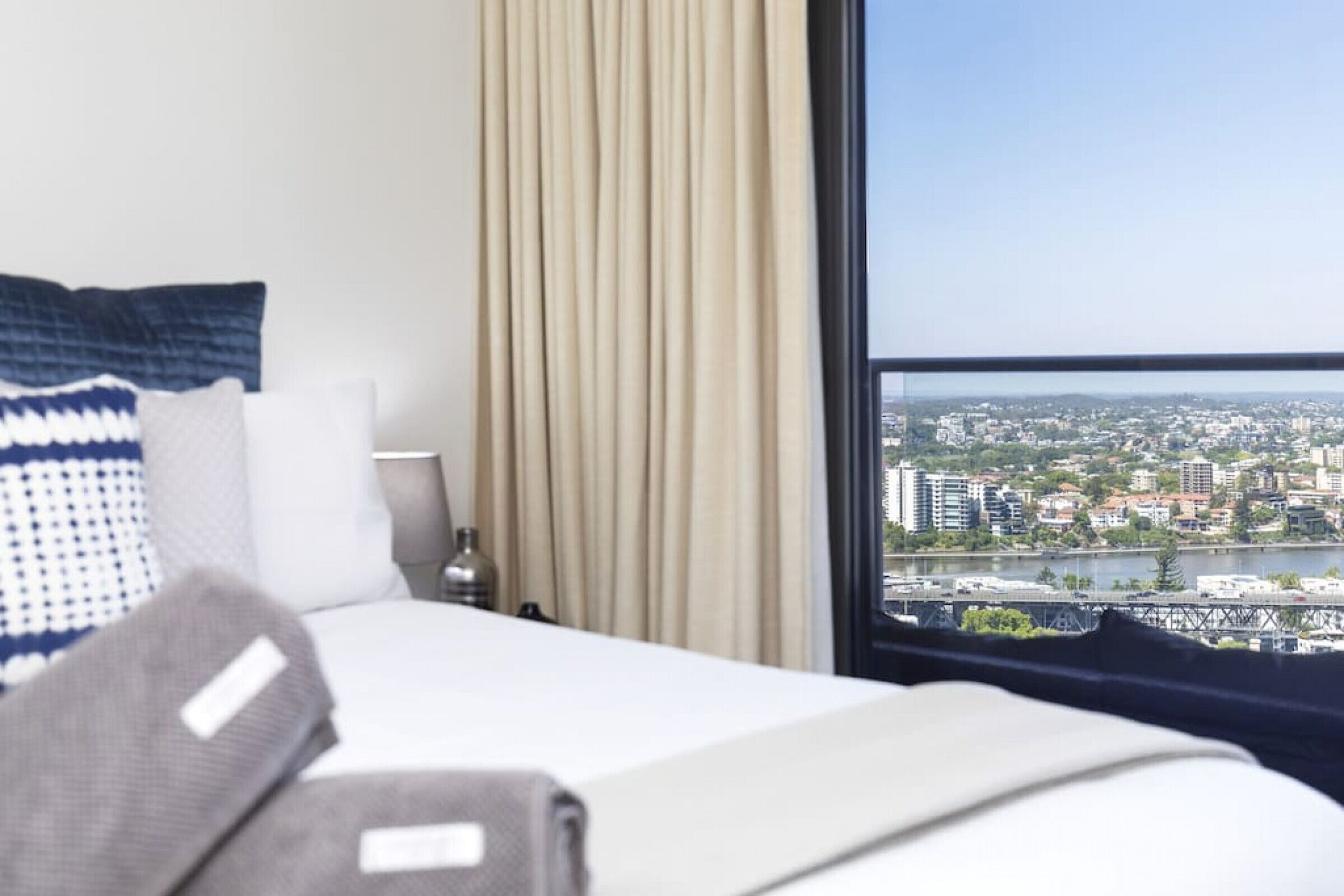 A hotel room with a bed, a view of a cityscape through a large window, and a curtain.