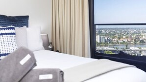 Une chambre d’hôtel avec un lit, une vue sur le paysage urbain par une grande fenêtre et un rideau.