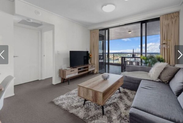 A modern living room with a sofa, a coffee table, a TV, and a balcony with a view.