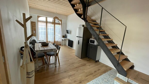 Een moderne keuken met een ingebouwde magnetron, een eethoek met een houten tafel en stoelen, en een trap met een houten afwerking.