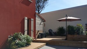 Een terras met een houten dek, een overdekte zithoek en een grote parasol.