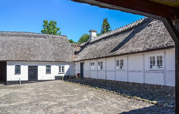 A traditional building with a thatched roof and white walls, a cobblestone courtyard, and a wooden door. - Nice home in Kirke Hyllinge with WiFi (Kirke Hyllinge)