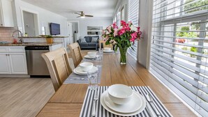 A dining area with a wooden table set for four, a vase of pink flowers, and a view of the outdoors through large windows. - Close to Beach & Shops | Private Home | Dog OK | Outdoor Seating | 1/2 mile to Siesta Key Bridge (Sarasota)