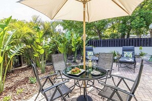 Une terrasse extérieure avec une table ronde, des chaises et un grand parasol.