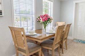 Une table à manger avec quatre chaises, un vase de fleurs et une fenêtre avec des stores.
