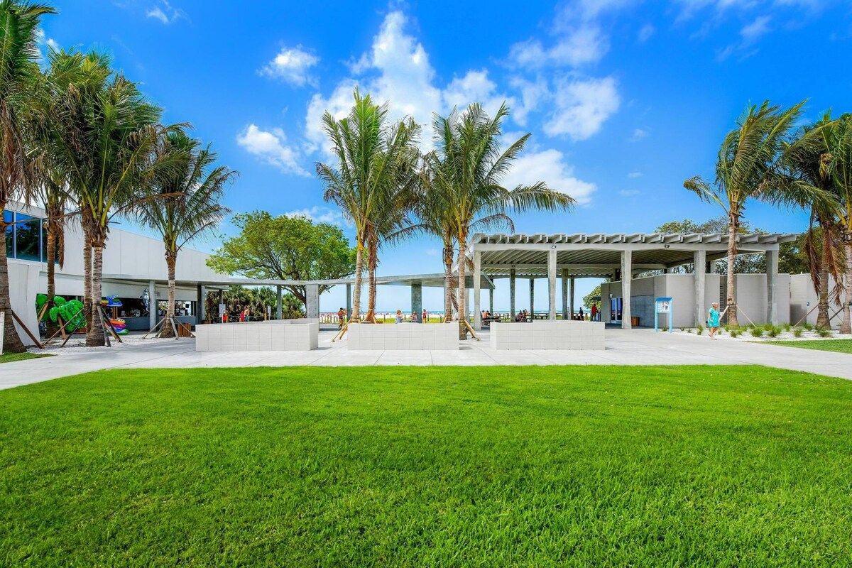 A modern building with a covered outdoor area, palm trees, and a well-maintained lawn.