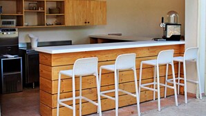 Una cocina compacta con armarios de madera, una encimera blanca y tres taburetes blancos.