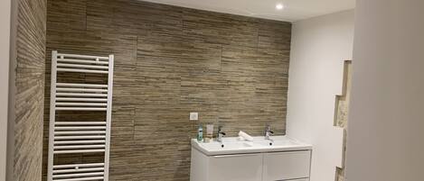 A modern bathroom with a wooden wall, a white sink with two basins, and a towel rack.