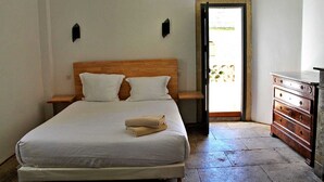 Un dormitorio con una cama, dos mesitas de noche, un aparador y una puerta que da a un balcón.