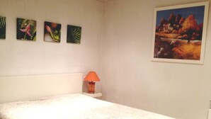 Une chambre à coucher avec un lit, une table de chevet avec une lampe et quatre tableaux encadrés accrochés au mur.
