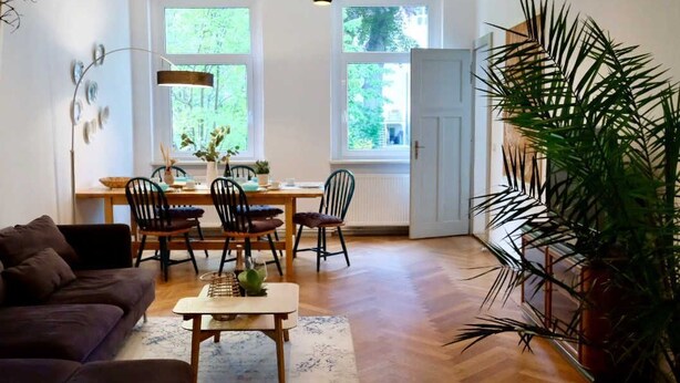 A spacious living room with a dark brown sofa, a wooden coffee table, and a large potted plant.