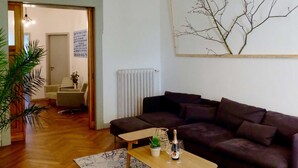 A living room with a dark brown sofa, a wooden coffee table with a bottle and glasses, and a patterned rug.