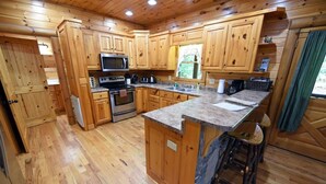 A wooden cabin-style kitchen with a central island, built-in appliances, and a window overlooking greenery. - Safe Haven- Mountain View-hot tub-wifi- pool table (Morganton)