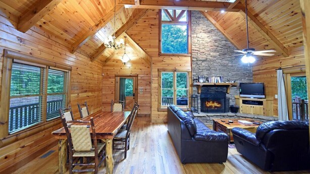 A log cabin interior with a dining area, a fireplace, a television, and a stone wall. - Safe Haven- Mountain View-hot tub-wifi- pool table (Morganton)