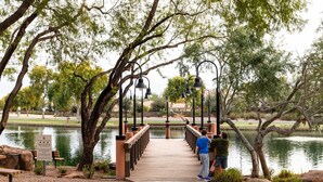 A wooden bridge over a lake with benches and lamp posts, surrounded by trees. - Cute, Clean & Comfortable in the Best Community! (Gilbert)