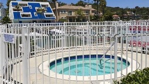Uma área de piscina cercada por grades de metal branco, com uma piscina azul cristalina e uma placa indicando zona proibida para natação.