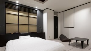 A modern hotel room with a large bed, a small table, and a window with blinds.