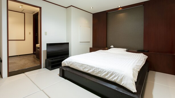 A modern bedroom with a large bed, a flat-screen TV, and a door leading to a bathroom.