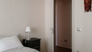 Un dormitorio con cama, una mesita de noche con lámpara, una puerta de madera y un interruptor de luz en la pared.