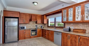 A modern kitchen with wooden cabinets, stainless steel appliances, and a tiled floor.