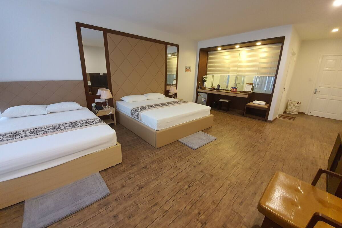 A hotel room with two beds, a desk, a chair, and a large mirror.