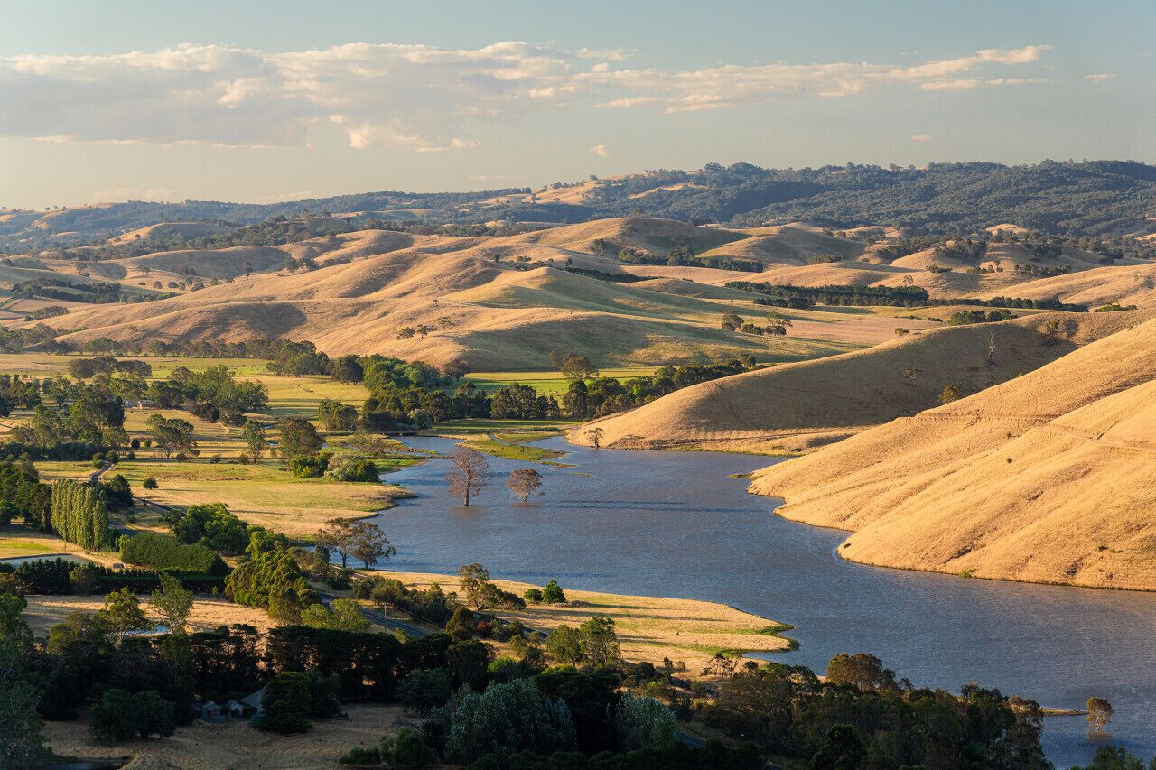 A river winding through rolling hills with sparse vegetation and a few scattered trees.