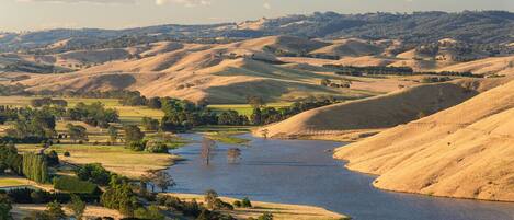 A river winding through rolling hills with sparse vegetation and a few scattered trees.