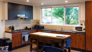 A modern kitchen with dark cabinets, a wooden table, and a window with a view of trees. - A perfect escape for couples & families & seniors (Bonnie Doon)