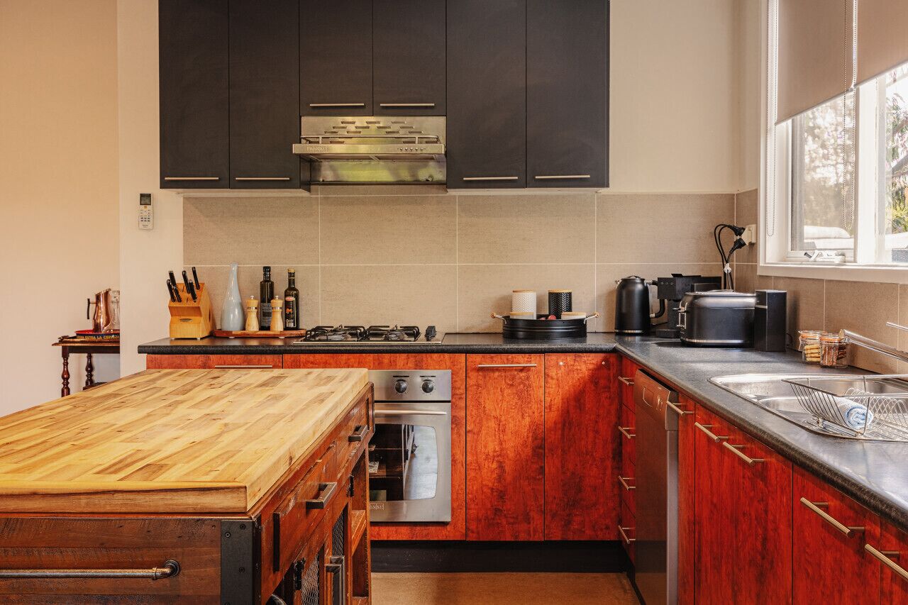 Una cucina moderna con mobili scuri, un piano di lavoro in legno, elettrodomestici in acciaio inossidabile e una finestra con vista.