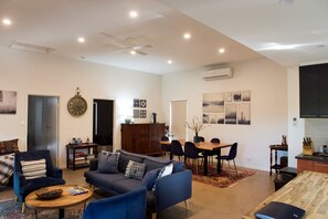 A living room with a sofa, chairs, a coffee table, a dining table with chairs, a clock, artwork on the wall, and an air conditioning unit. - Pet friendly rural escape for couples & families (Bonnie Doon)