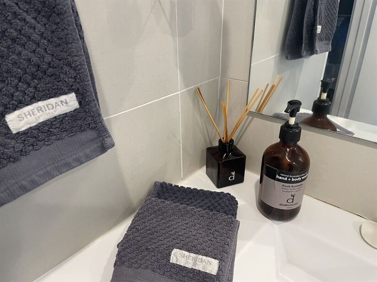 A bathroom with a towel rack, a bottle of hand and body wash, and a small black container with reed diffusers.