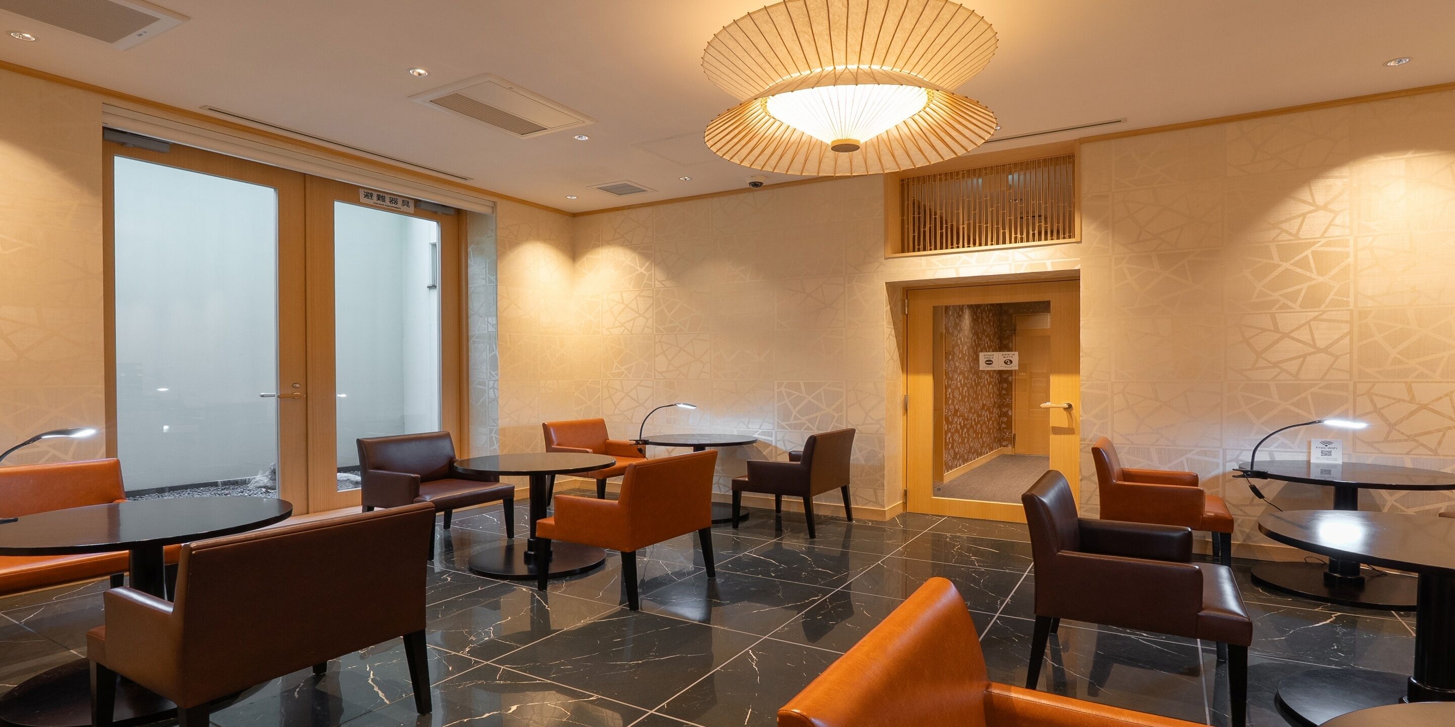 A hotel lobby with multiple seating areas, including round tables and cushioned chairs, and a large decorative light fixture on the ceiling.
