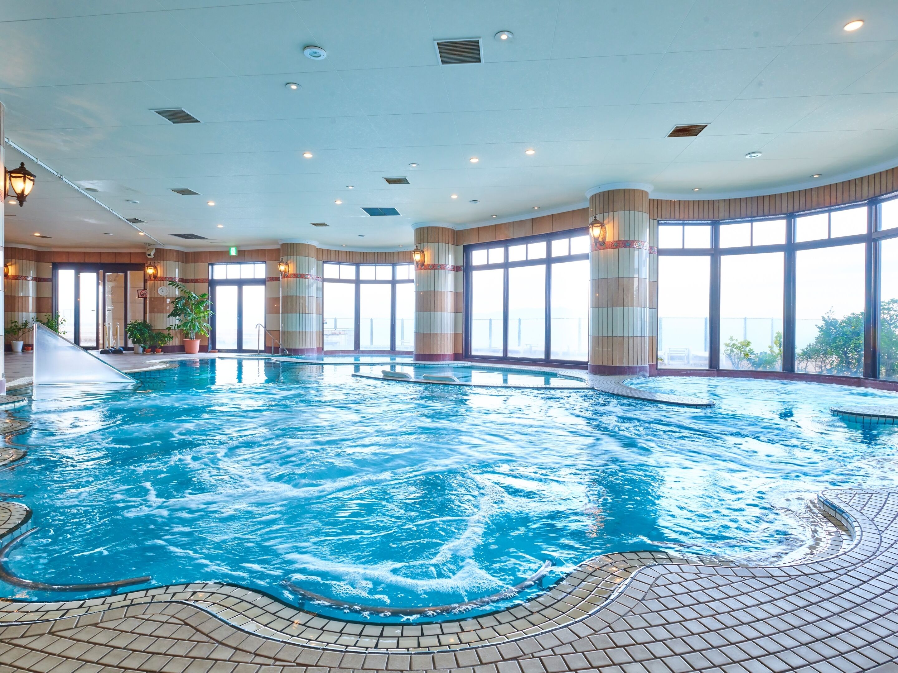 Une piscine intérieure dotée d’un sol carrelé, de grandes fenêtres et de colonnes.