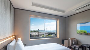A hotel room with a large bed, a view of the sea, a desk, and a chair. - Enoshima Hotel (Fujisawa)