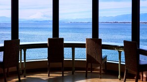 A room with three wicker chairs facing a large window overlooking a body of water and distant mountains. - Enoshima Hotel (Fujisawa)