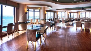 A spacious dining area with high tables and wicker chairs, large windows offering a view of the sea, and a modern ceiling design. - Enoshima Hotel (Fujisawa)