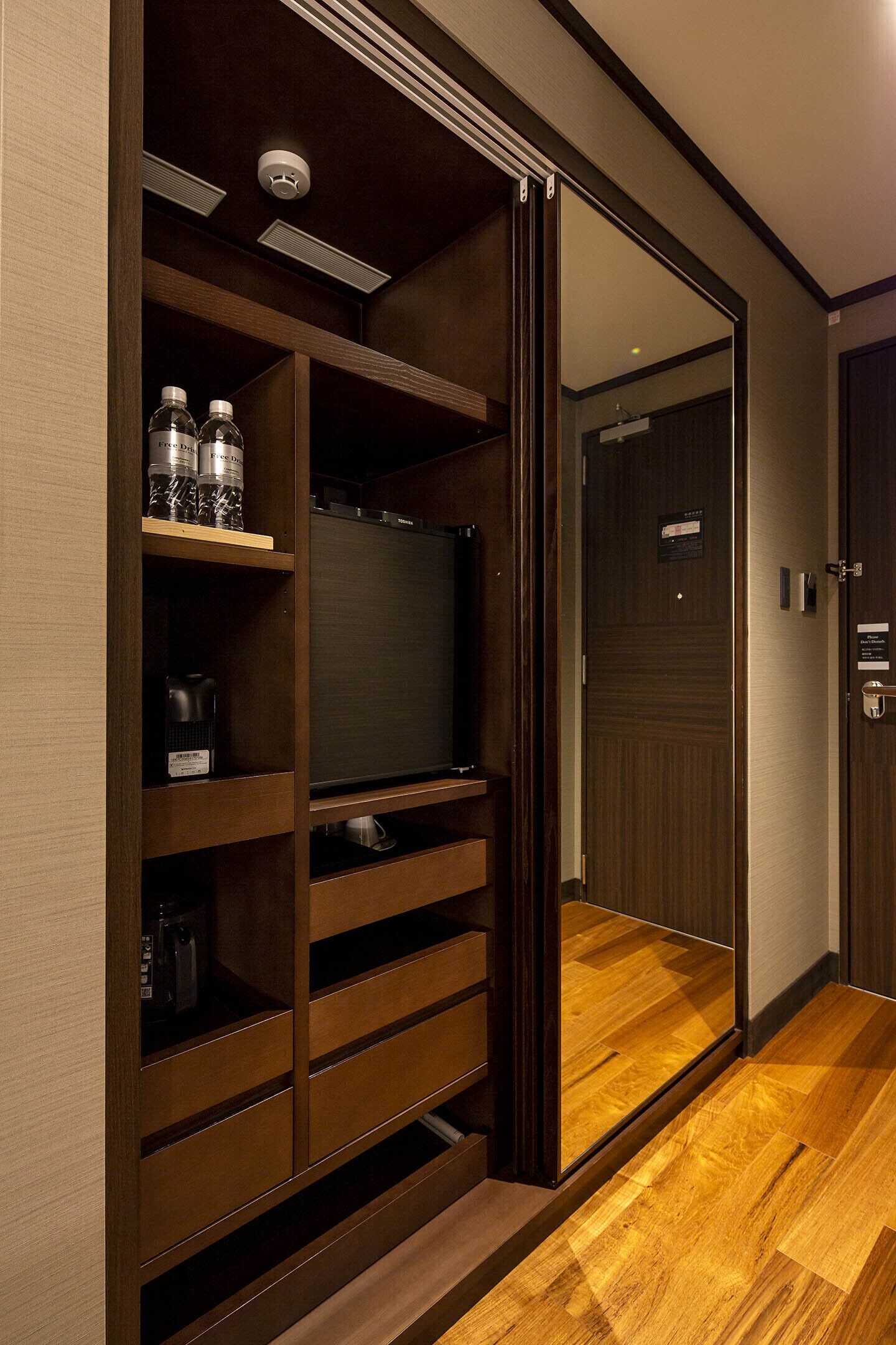A wooden entertainment unit with a television, shelves with bottles, and a coffee maker.