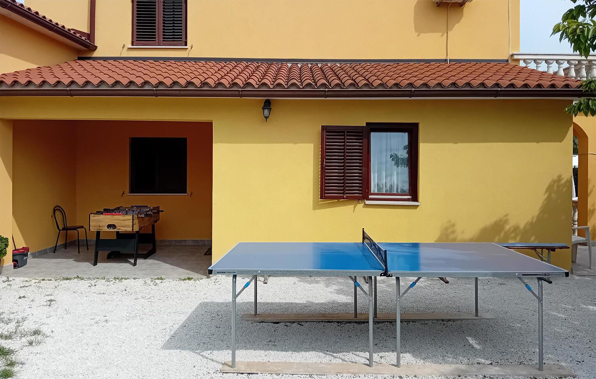 Un edificio amarillo con techo de tejas rojas, una mesa de ping-pong y una mesa de futbolín en el exterior.