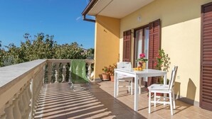Un balcon avec une table et des chaises, des plantes en pot et une vue sur les arbres.