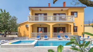 Un bâtiment jaune à deux étages, doté d’une piscine et d’un espace extérieur aménagé pour s’asseoir.
