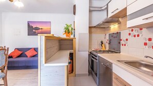 Une cuisine compacte équipée d’une cuisinière, d’un four et de meubles de rangement modernes. On aperçoit à l’arrière-plan un coin repas avec un canapé et un tableau.