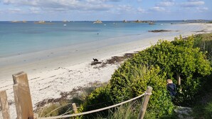 A beach with clear skies, calm waters, and distant rocky outcrops.