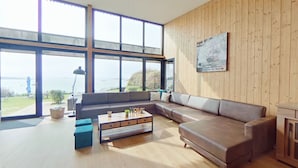 A modern living room with large windows, a wooden wall, and a view of the outdoors.