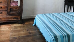 Ett rum med en garderob i trä, en säng med ett randigt överkast, en växt som hänger på väggen och ett litet bord med en lampa.