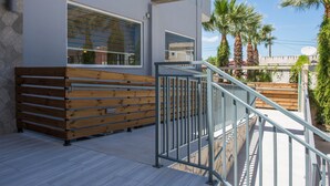 A modern building with a wooden bench and metal railing, overlooking palm trees and a clear sky. - Hotel Alexander the Great (Zakynthos)