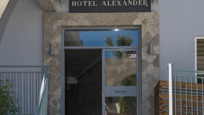 A hotel entrance with a stone facade, a sign reading "HOTEL ALEXANDER," and a set of marble stairs with metal railings. - Hotel Alexander the Great (Zakynthos)