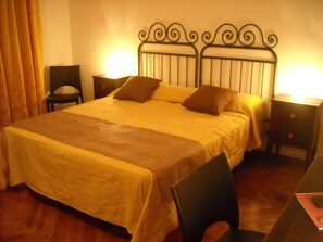 Una cama bien hecha con cabecera, una silla, una mesita de noche y una lámpara.