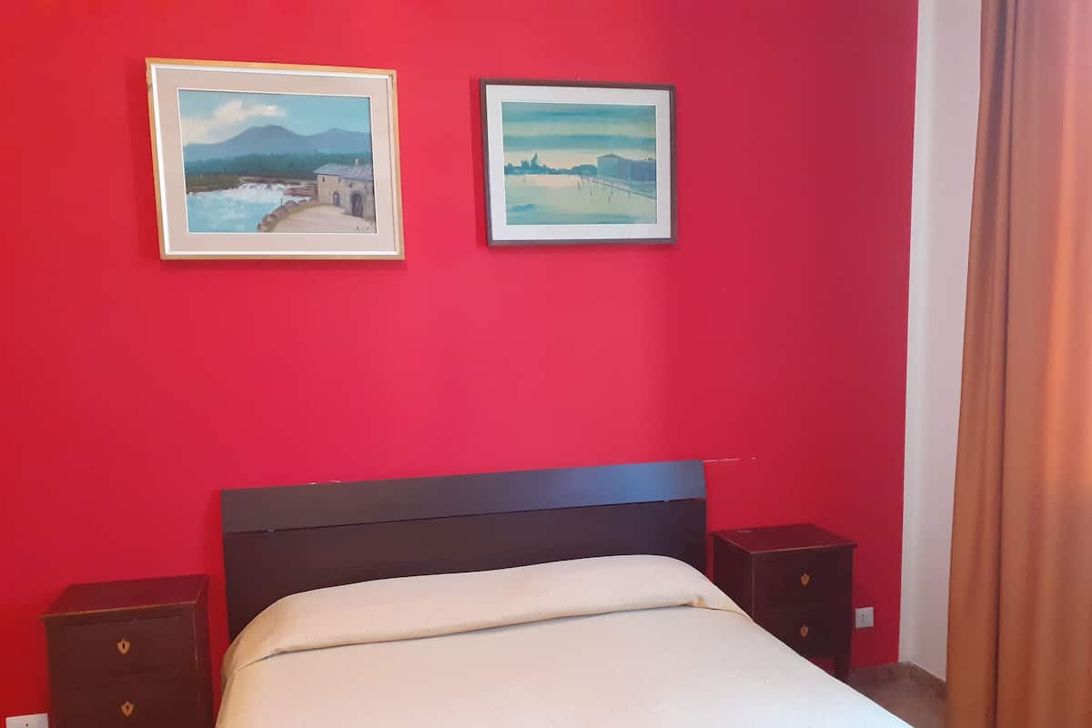 Une chambre d’hôtel avec un mur rouge, un lit recouvert d’une couette blanche, deux tables de chevet et deux tableaux encadrés.